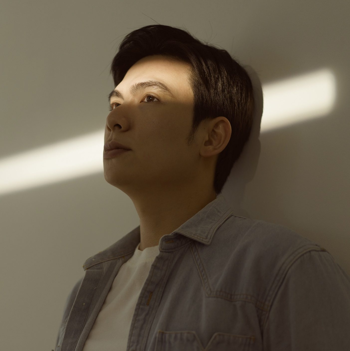 Man in Denim Shirt Ponders Under Sunlight in Minimalist Setting 01/05/2025