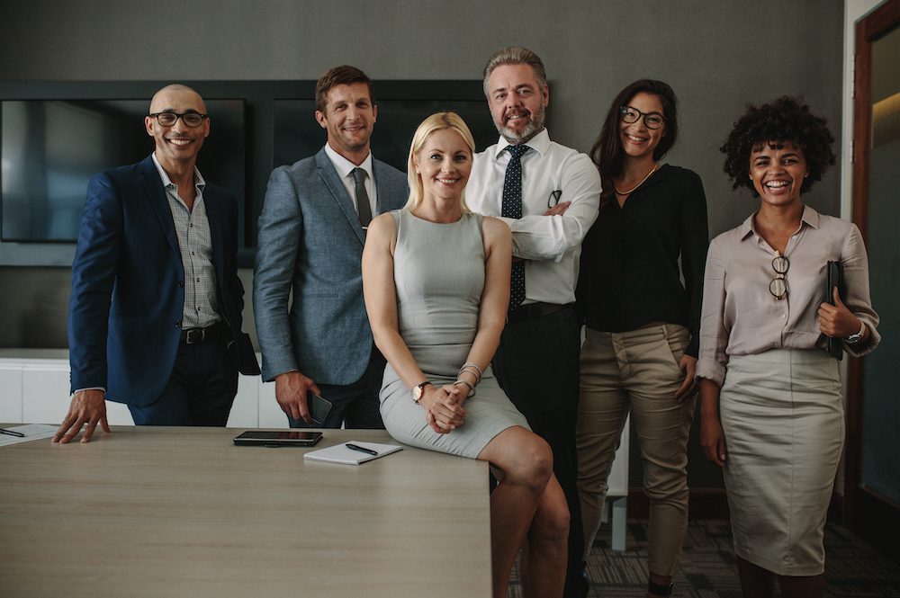 Portrait of diverse business professionals together in office meeting room. Team of corporate professionals looking at camera and smiling in board room.
