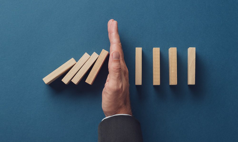 Top view of business crisis manager stopping falling dominos from collapsing. Over navy blue background.