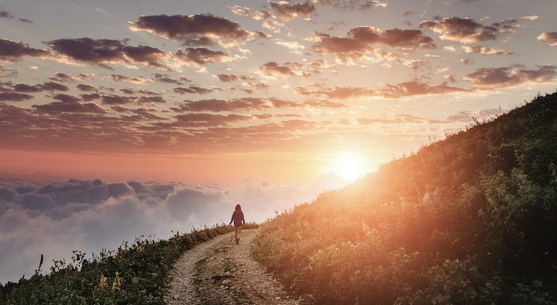 Woman on trail admiring the sunset with clouds and fog.